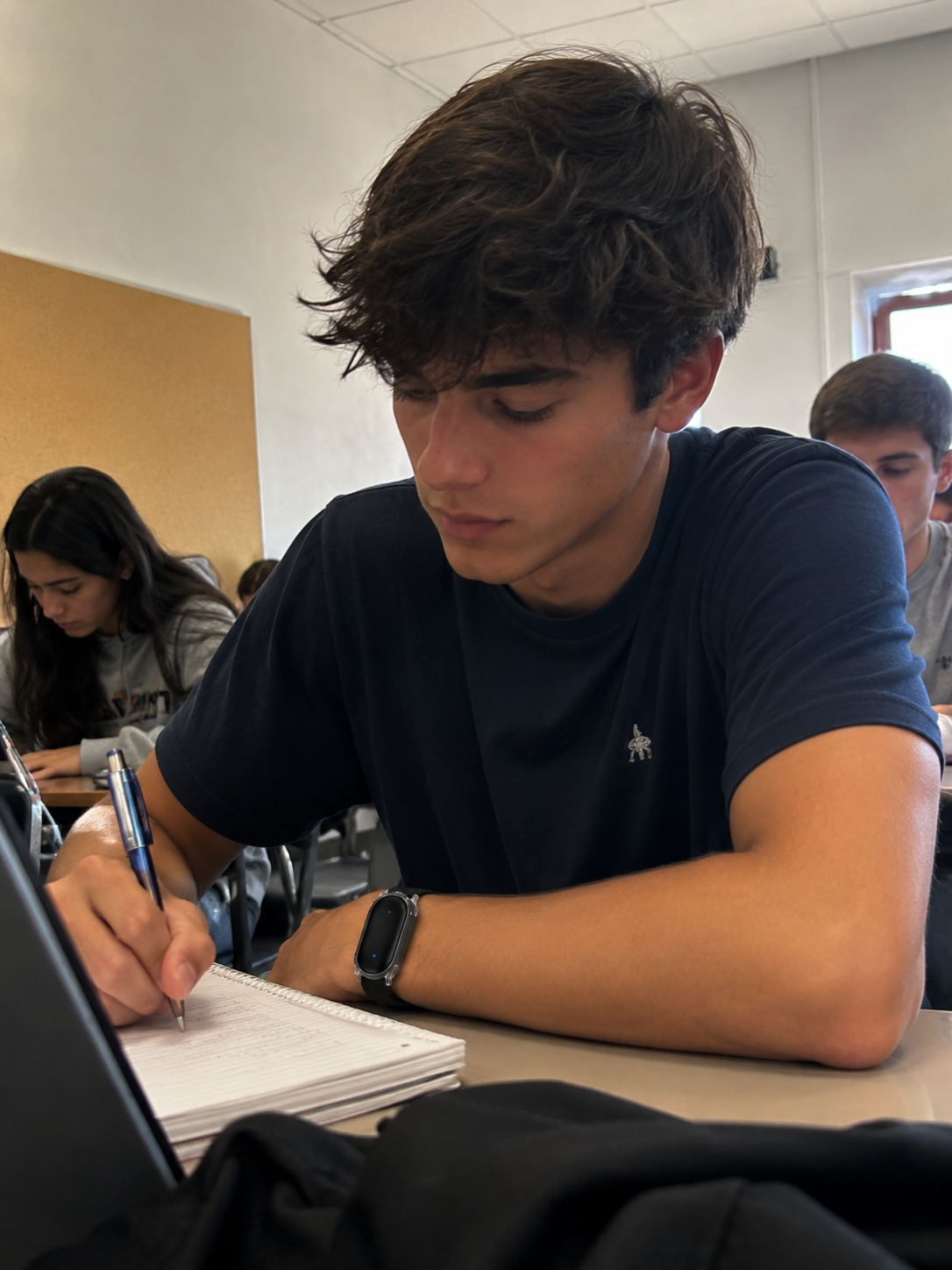 Student writing in a notebook wearing Trace, classroom setting